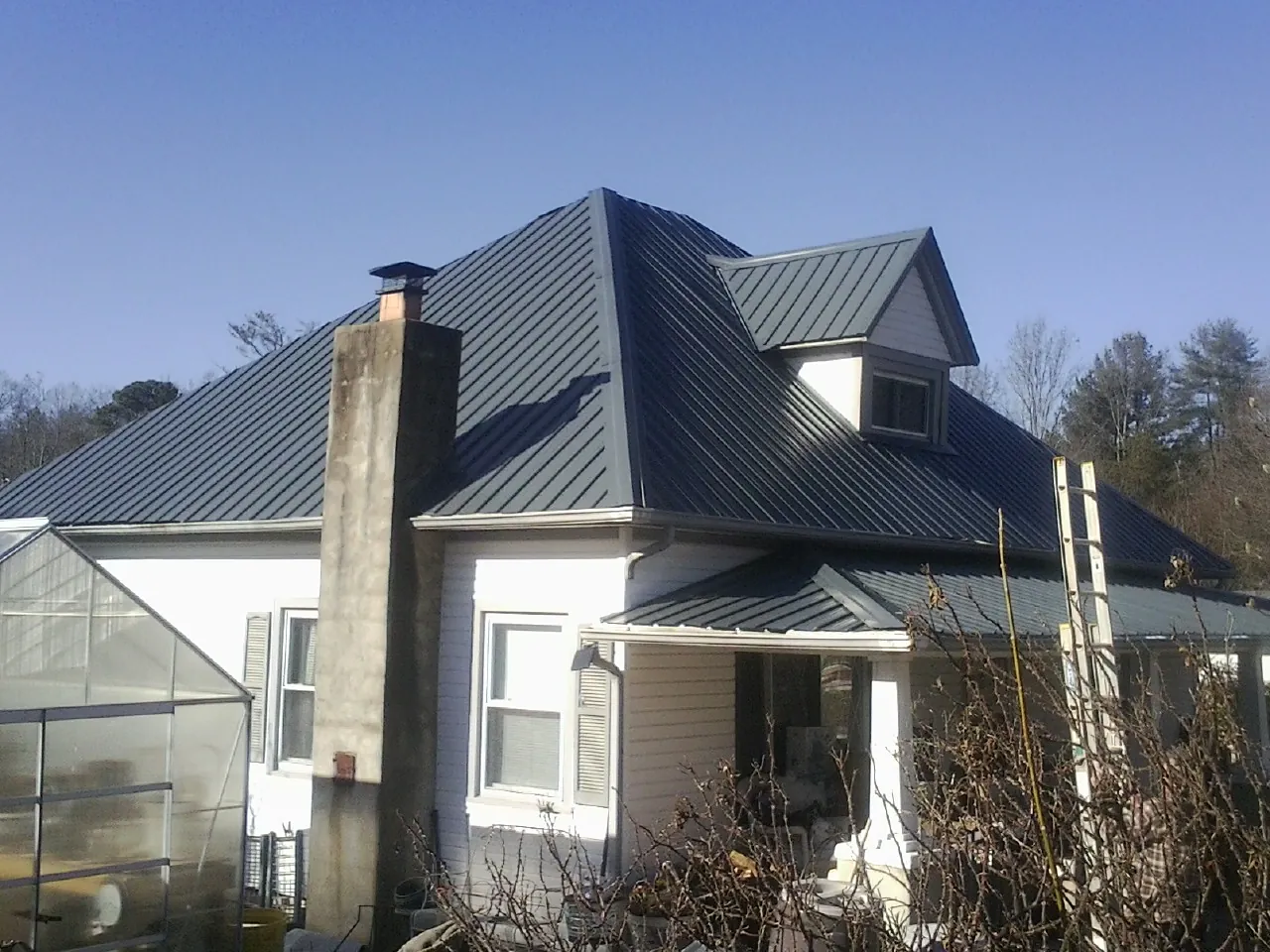 Dark blue standing seam metal roof on a white farmhouse with dormer — Slate & Tile Roof Repair by Roofing Brothers in Chesterhill
