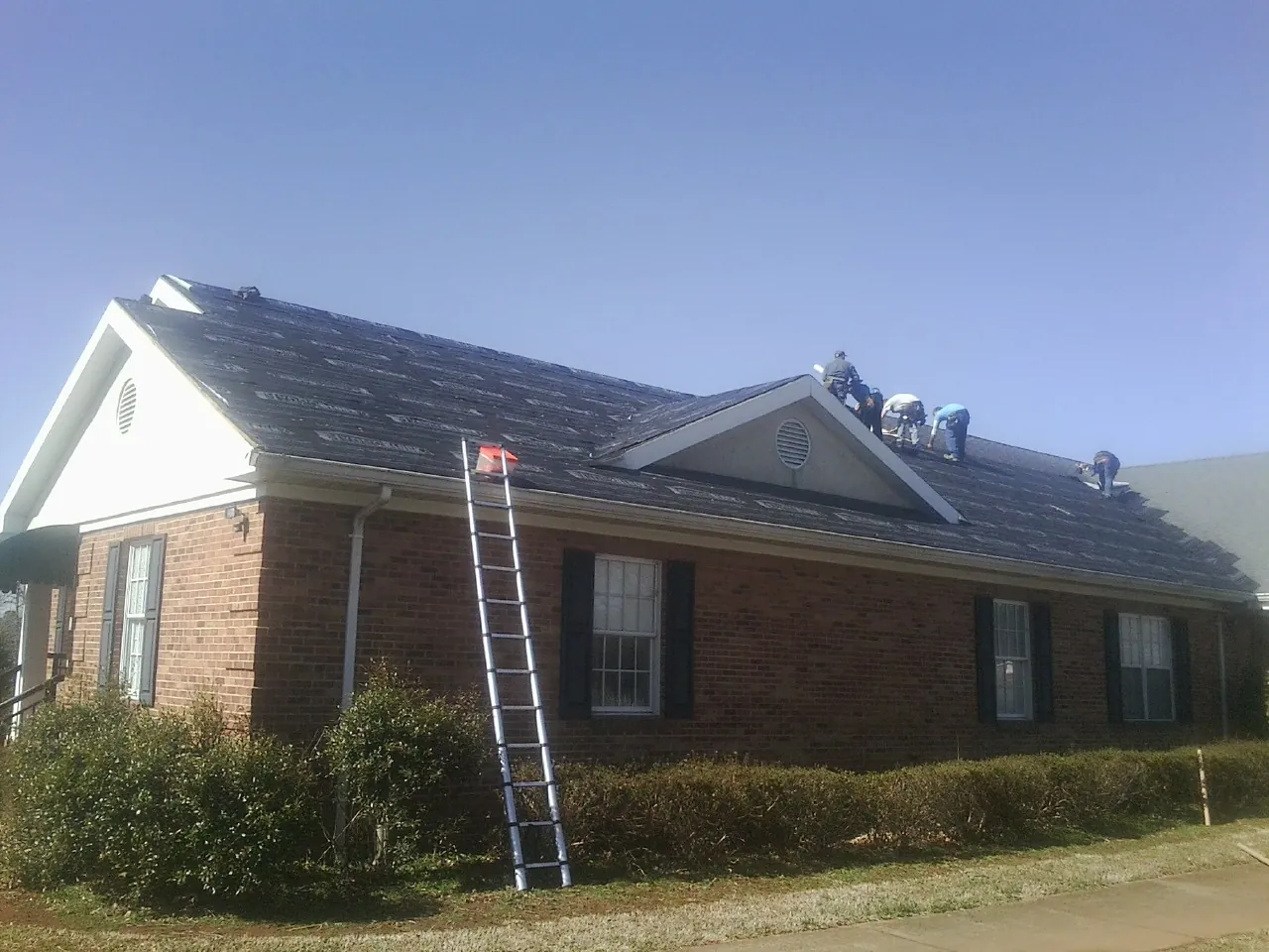 Crew tearing shingles off a brick ranch roof with a ladder set — Emergency Roof Repair work by our crew in Chesterhill