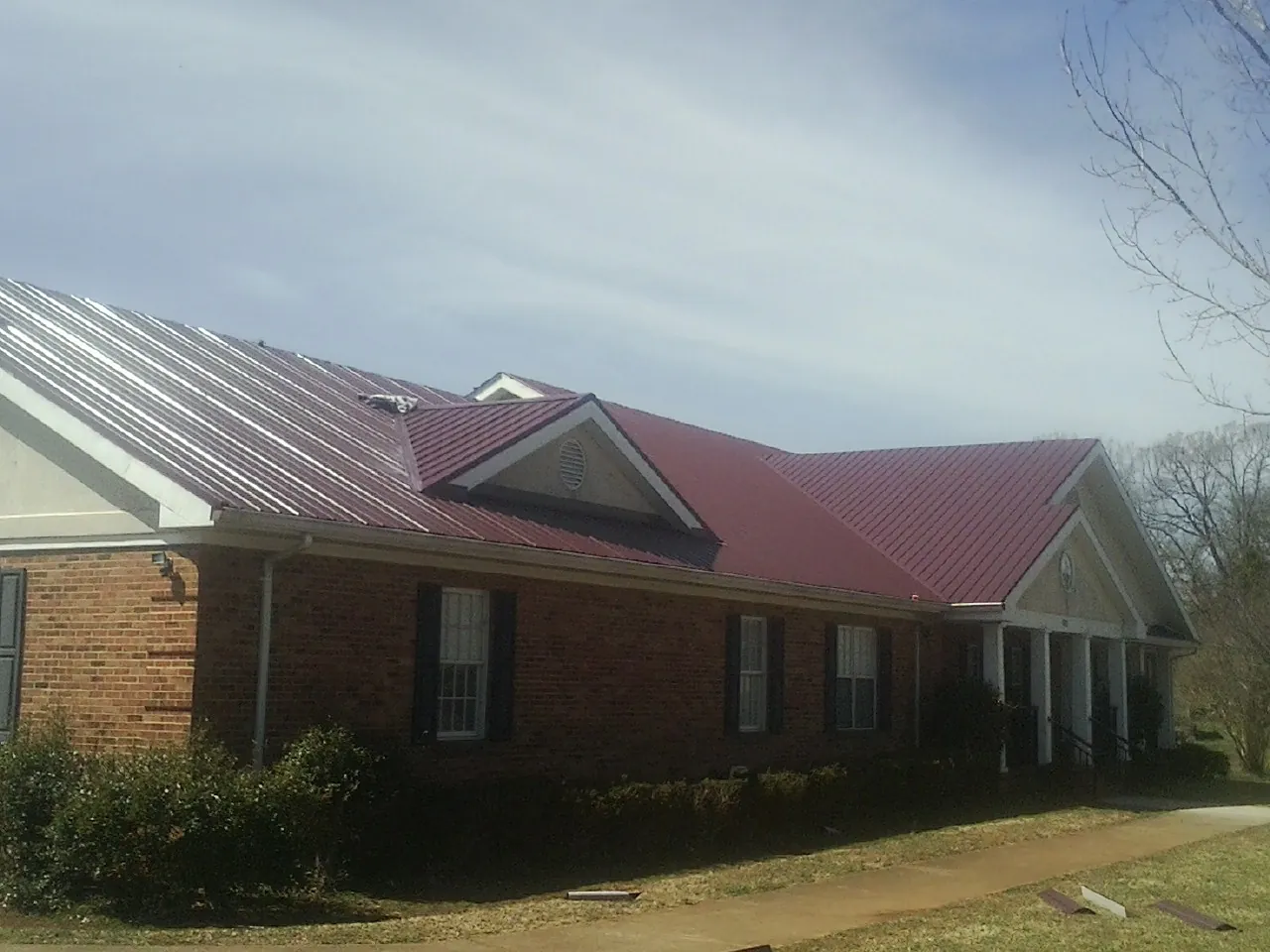 Red metal roof with gabled entries on a long brick building, from a Hail Damage Roof Repair job in Chesterhill