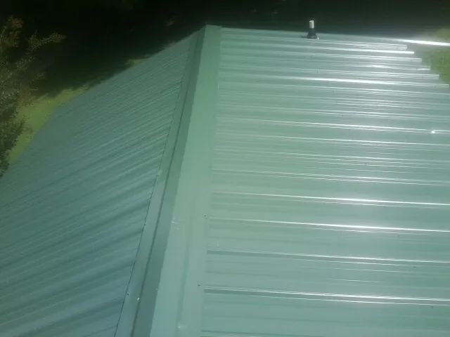 New green metal panels meeting at the ridge of a roof — Flat Roof Repair work by our crew in Chesterhill