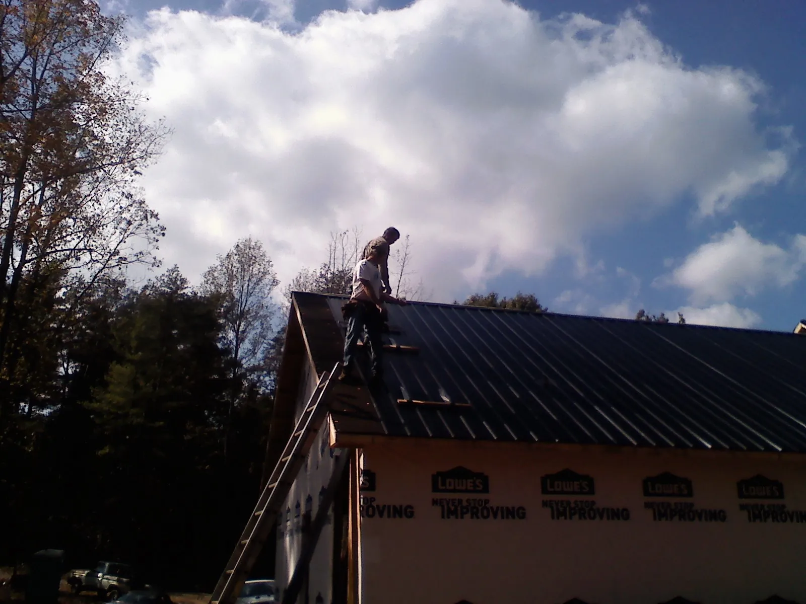 Roofer fastening dark metal panels high against a cloudy sky, from a Roof Inspection job in Chesterhill
