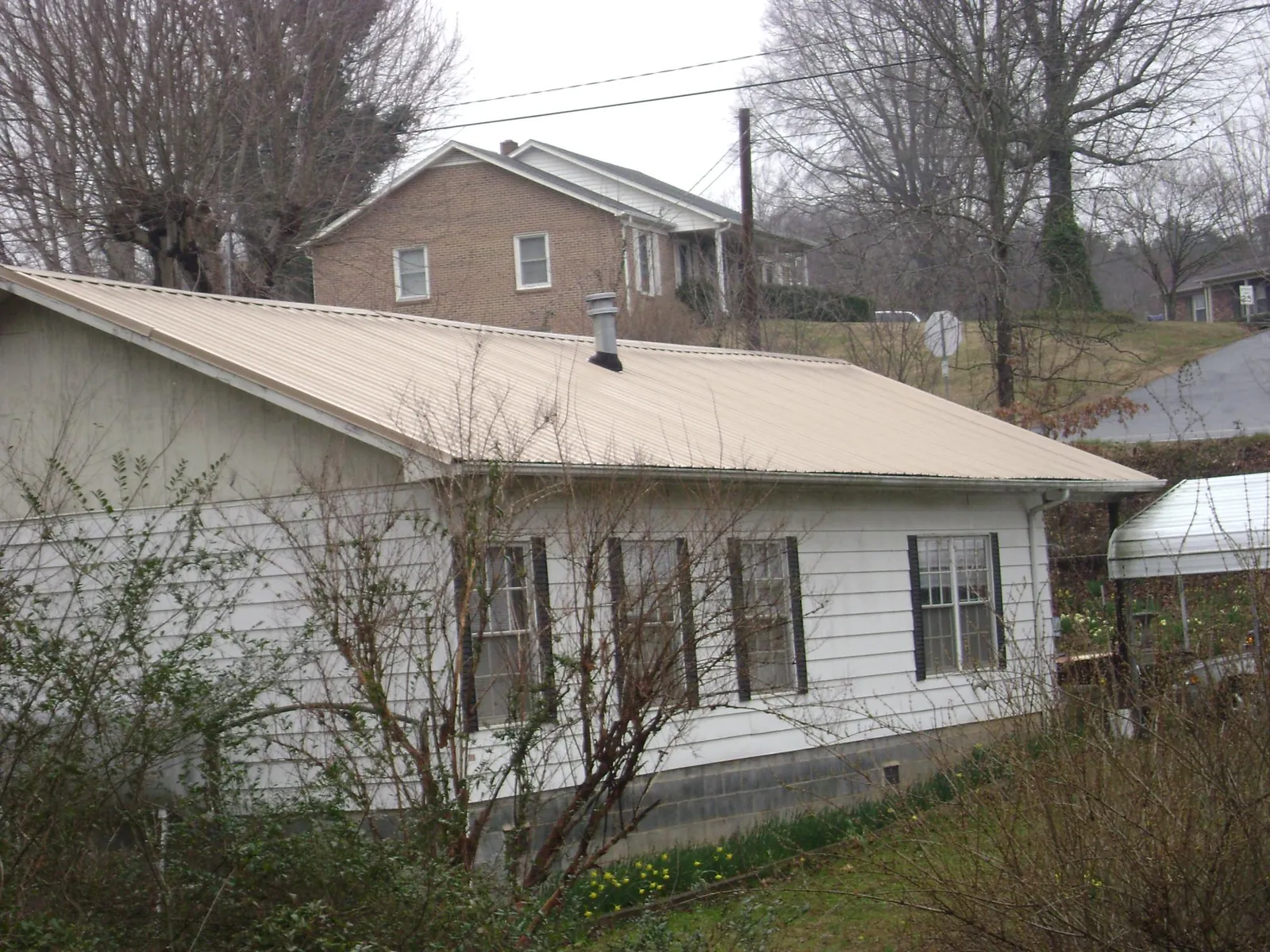 Tan metal roof on a white sided house set into a hillside — Commercial Roofing by Roofing Brothers in Chesterhill