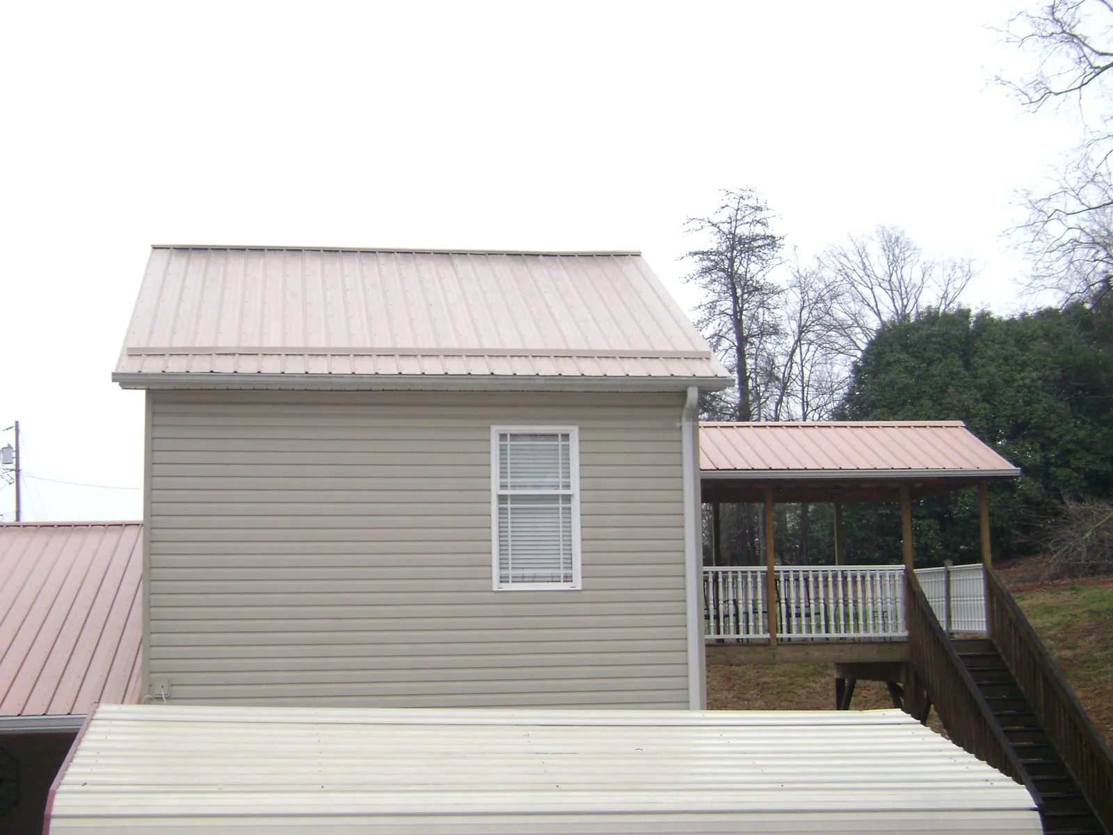 Tan metal roofs on a two story addition and attached porch, from a Roof Replacement job in Chesterhill